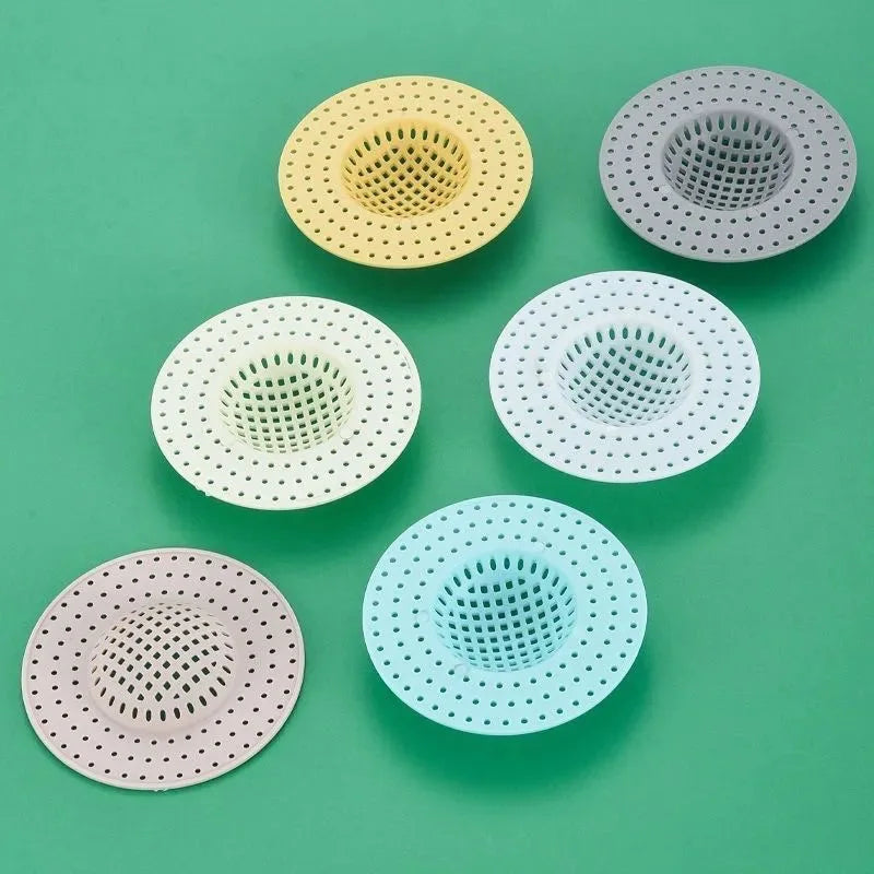 A collection of five circular kitchen sink drain strainers or hair catchers in various pastel colors including yellow, gray, 