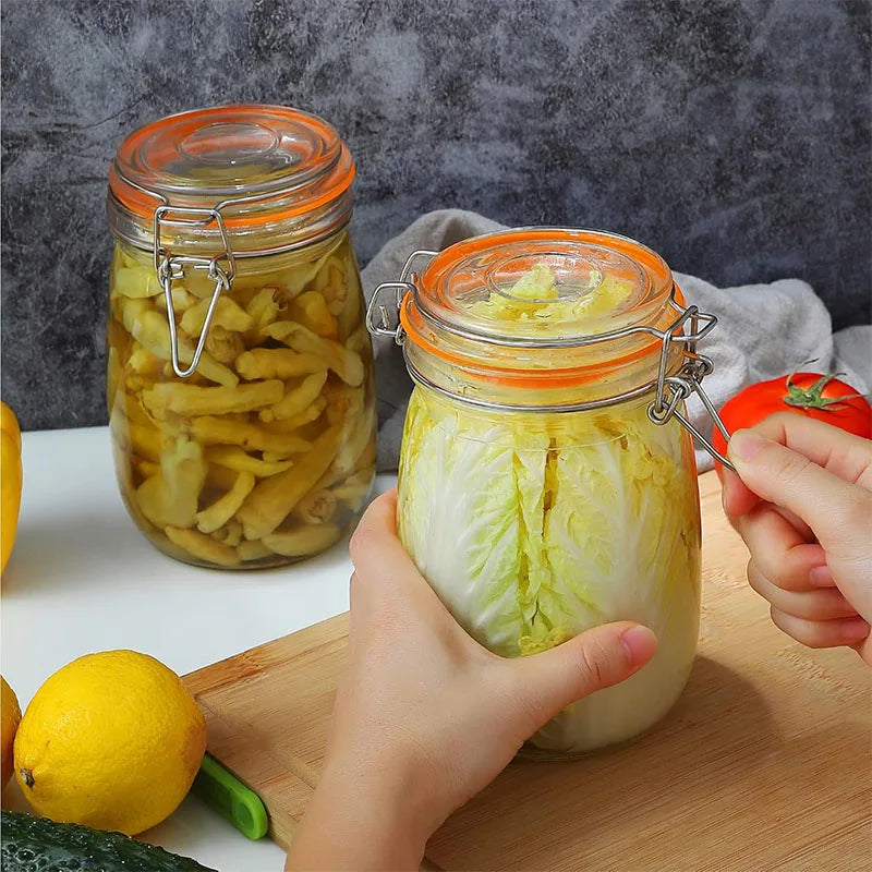 Hands are squeezing a large glass mason jar filled with sliced cucumbers and a lemon on a wooden cutting board.