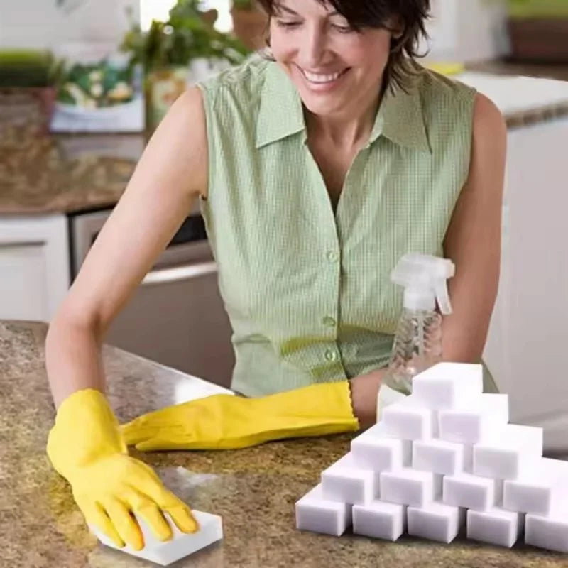 A woman wearing a yellow glove is preparing to use white magic cleaning sponges on a kitchen counter.