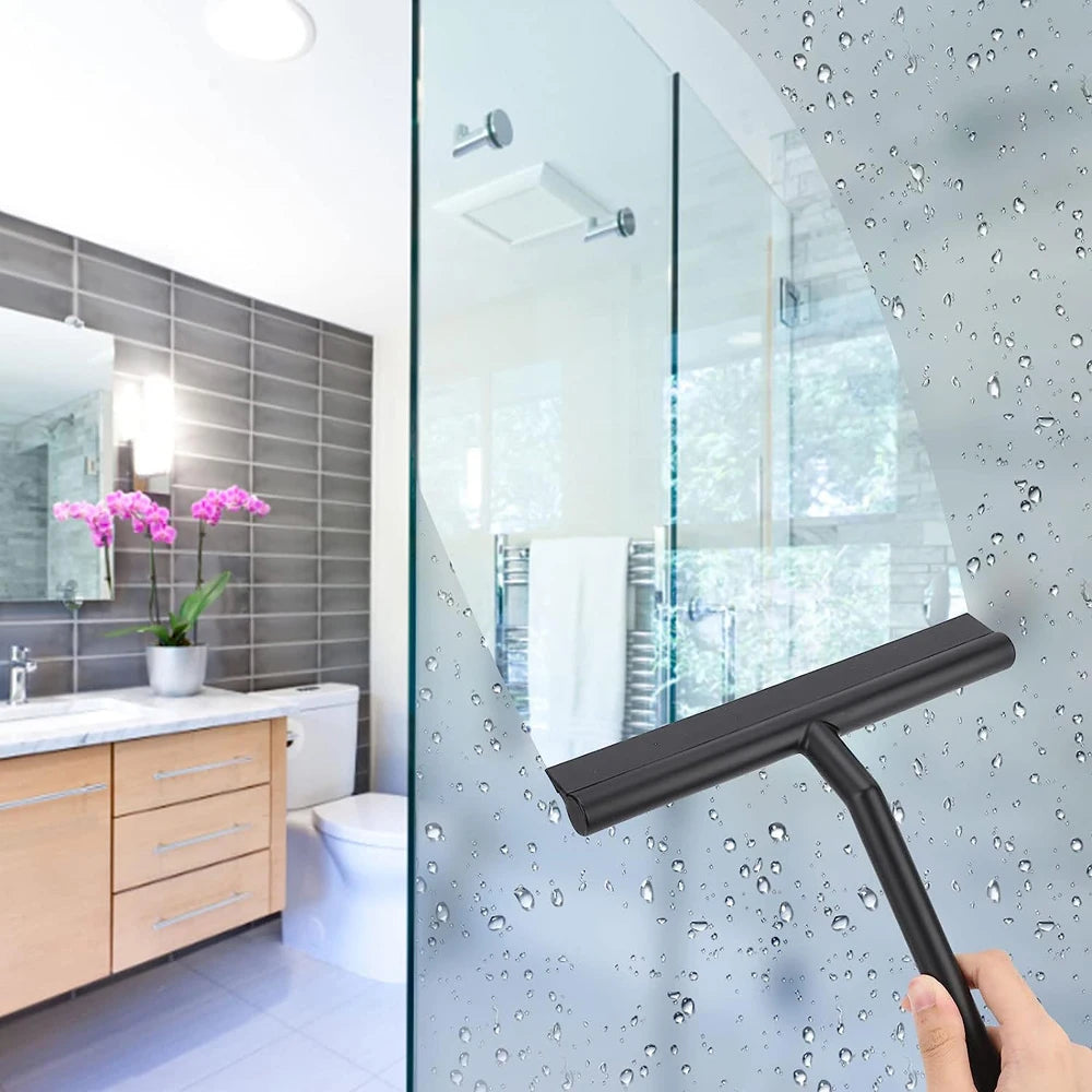 A hand uses a black silicone shower squeegee to clean condensation and water spots from a glass shower door.