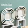 A foldable plastic wash basin in white and light blue is shown with various items inside on a wooden surface.