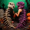 A person wearing a realistic dinosaur skeleton costume, featuring a gray skull and purple rib cage, posing in an outdoor sett
