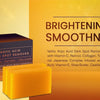 Une boîte marron foncé et une barre de savon Kojic Acid Dark Spot Remover jaune sont présentées sur un fond orange.