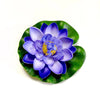 A vibrant purple artificial lotus flower with blue petals and yellow center resting on a green leaf.