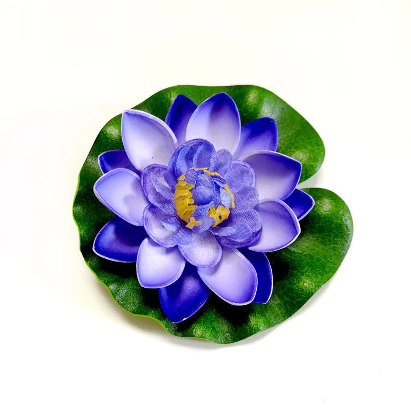 A vibrant purple artificial lotus flower with blue petals and yellow center resting on a green leaf.
