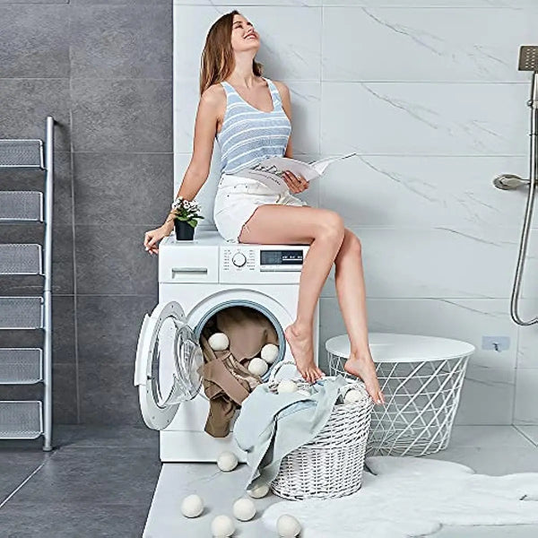 A woman is sitting on a washing machine, surrounded by reusable wool dryer balls and laundry.