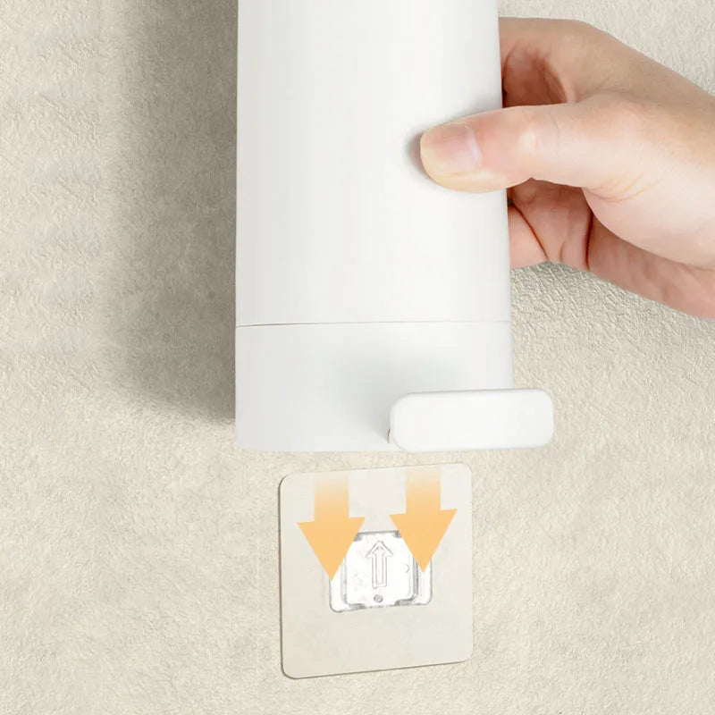 A hand is installing a white portable soap bar grinder with a wall-mount design onto a light-colored wall.