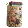 A beige quilted laundry basket with handles filled with folded purple and green fabric.