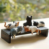 A set of four cute healing cat figurines in various colors and breeds displayed on a dark wooden plank.