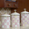 Three pastel pink and cream checkered storage jars with gold lids on a light surface.