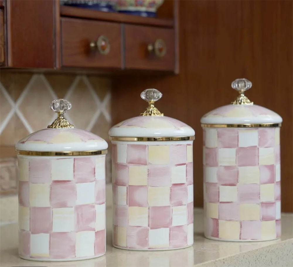 Three pastel pink and cream checkered storage jars with gold lids on a light surface.