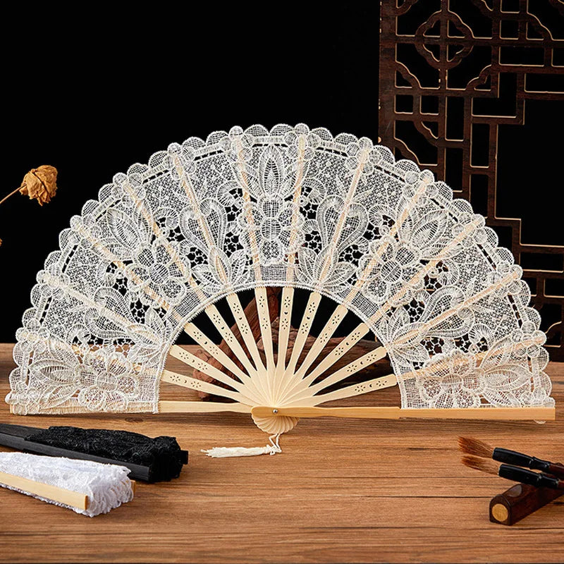Elegant lace folding handheld fan with a white and beige design displayed on a wooden surface.