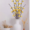 Eine Vase mit Ästen künstlicher gelber Pflaumenblüten und getrocknetem Gras als Heimdekoration.