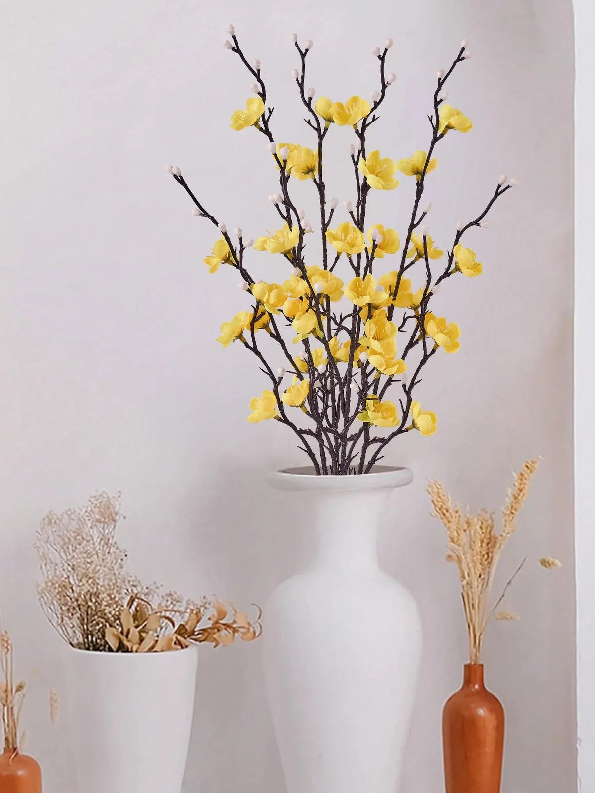 Eine Vase mit Ästen künstlicher gelber Pflaumenblüten und getrocknetem Gras als Heimdekoration.
