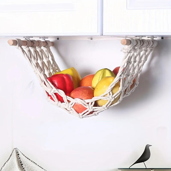 A woven sisal fruit hammock storage basket filled with colorful fruits hanging from a shelf.