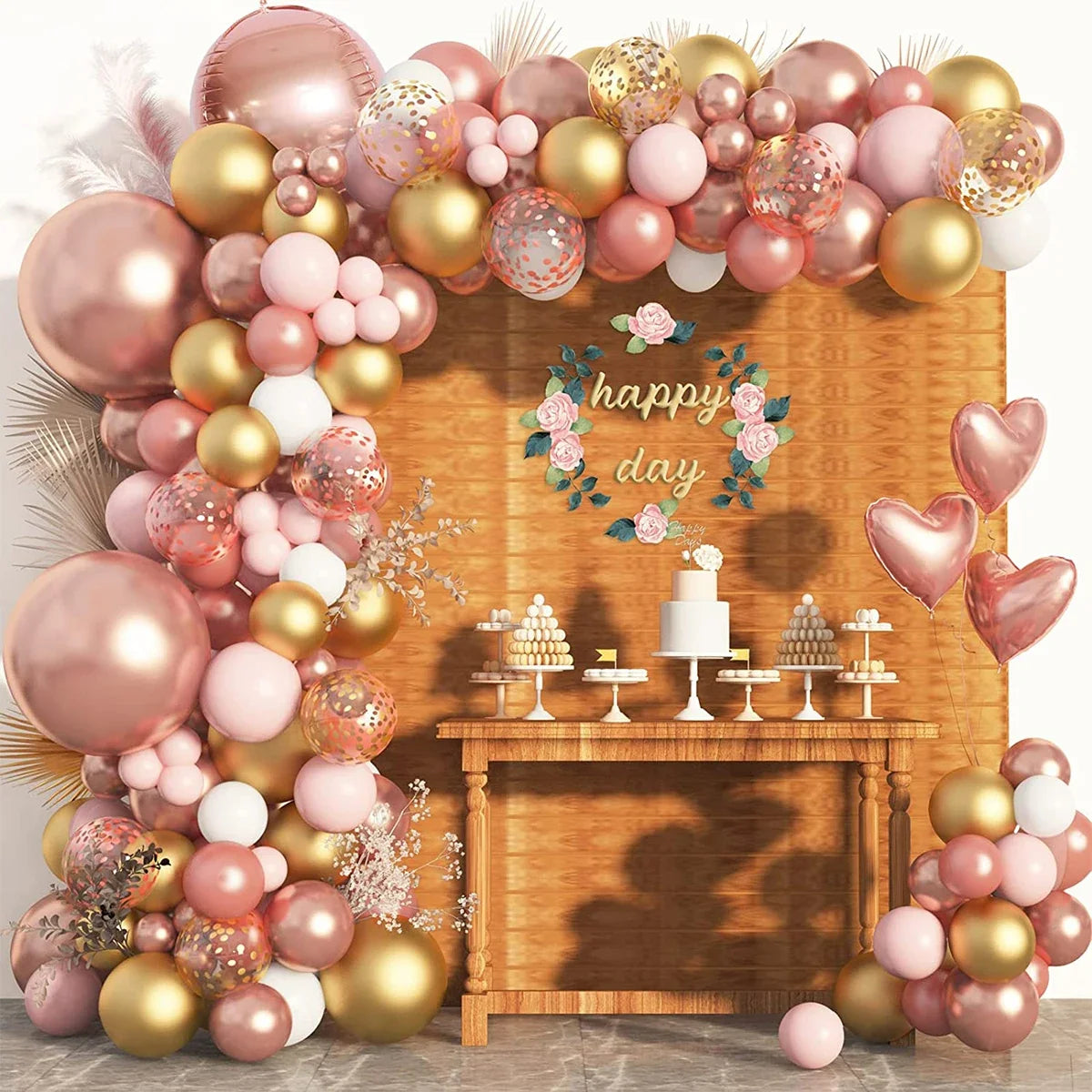 A pink and gold foil balloon garland decorated with hearts and greenery, displayed against a wooden background.