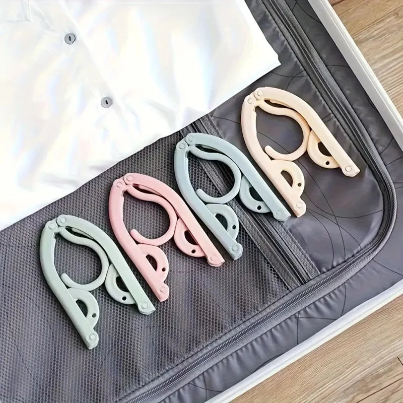 A set of five portable foldable clothes hangers in pastel colors, including pink, mint green, and beige, resting on a gray fa