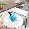 A hand is using a blue sponge brush on a white plate in a kitchen sink to clean dishes.