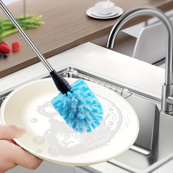 A hand is using a blue sponge brush on a white plate in a kitchen sink to clean dishes.