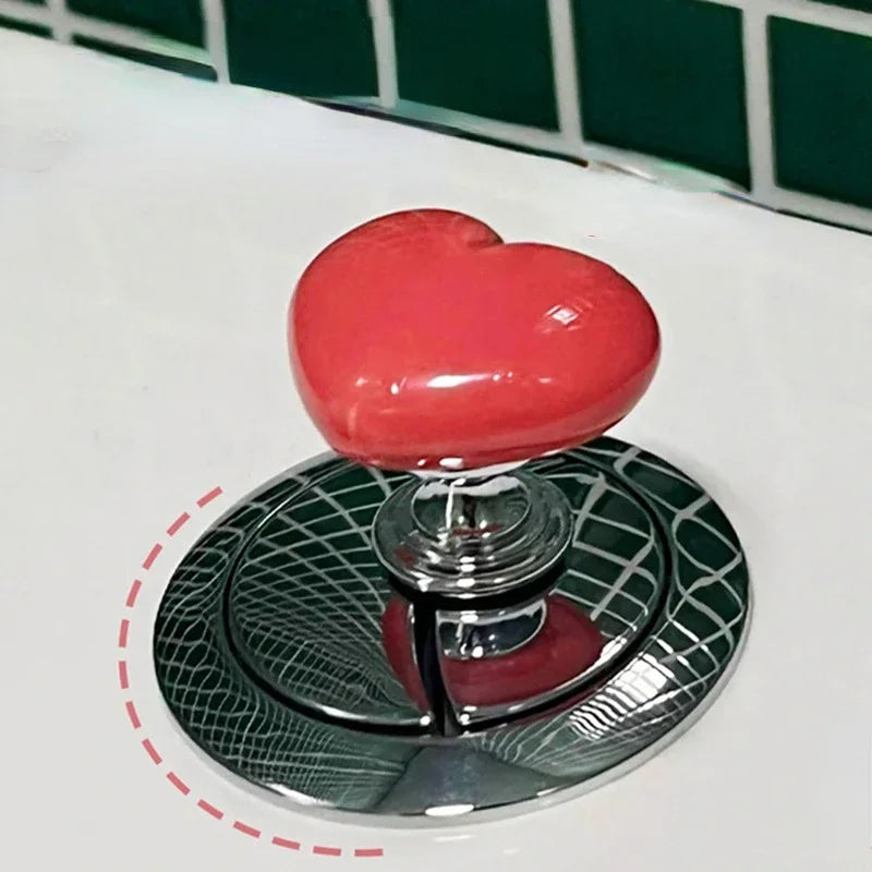 Bouton de chasse d'eau en forme de cœur rouge sur une plaque argentée décorative.