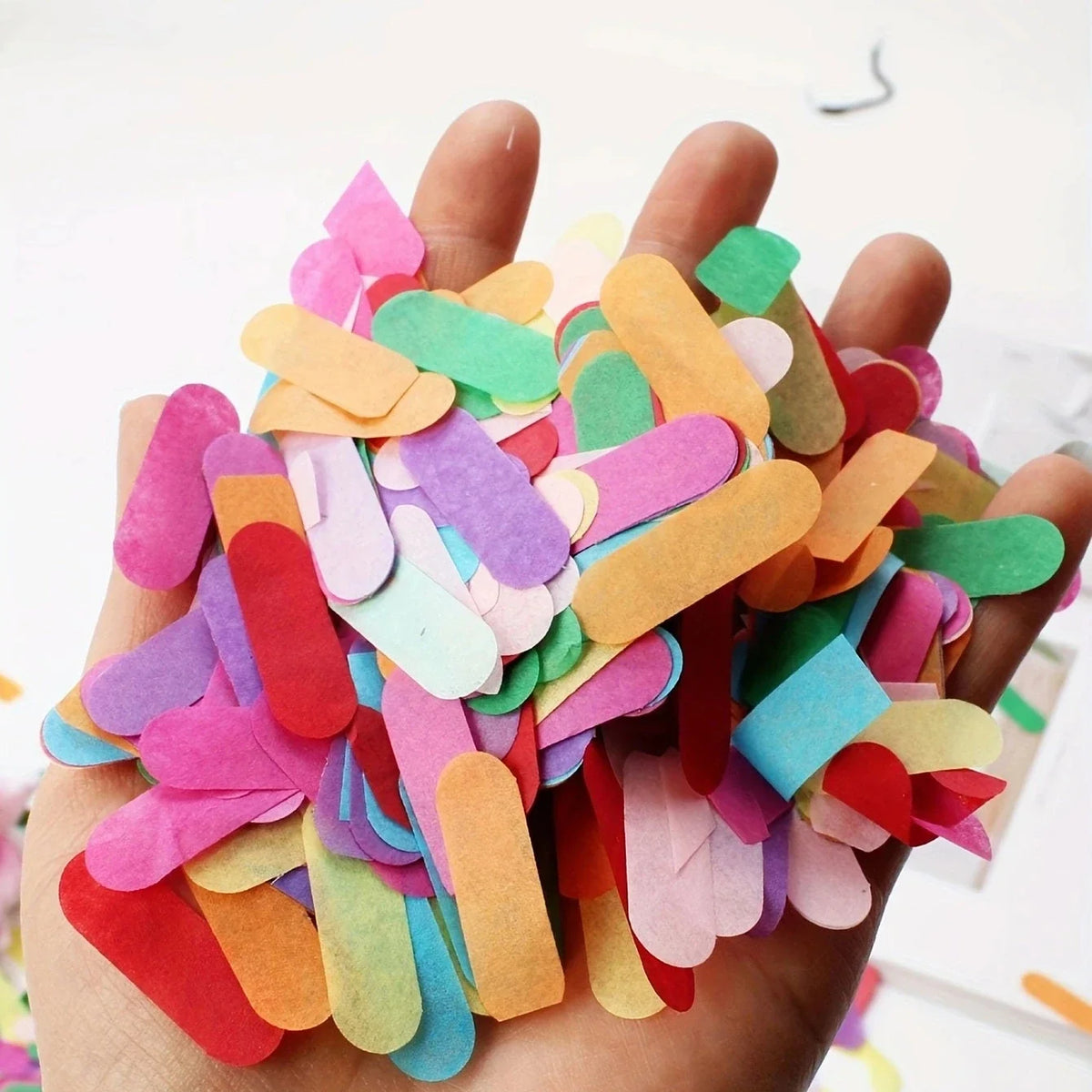 A hand holds a colorful confetti decoration set consisting of various colored paper pieces.