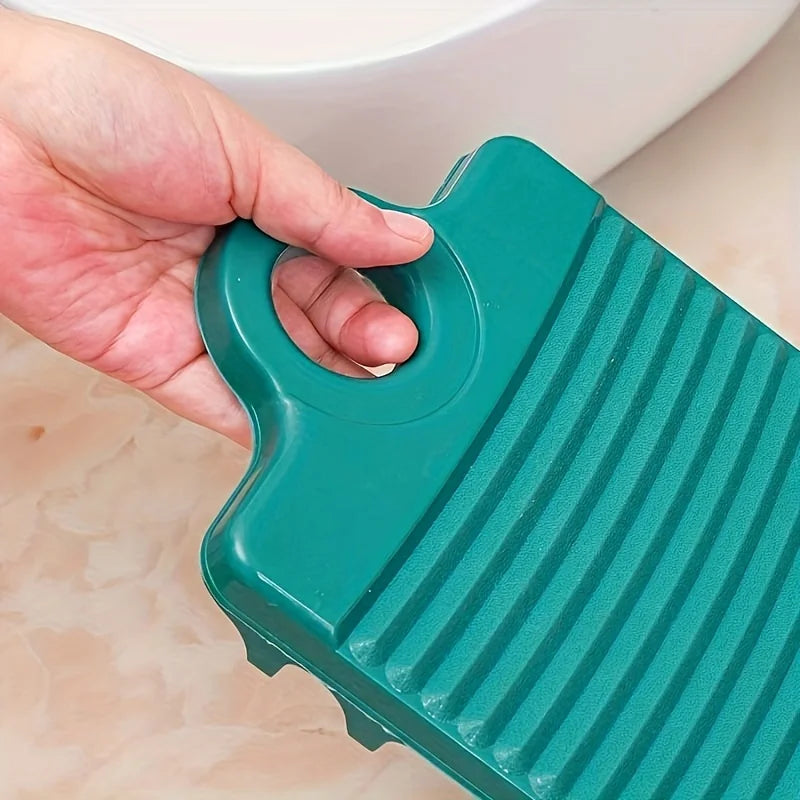 A hand holds a teal portable anti-slip wash basin with ridges, positioned above a white ceramic basin.