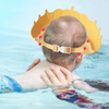 A baby is shown wearing a yellow, adjustable bath shampoo shield cap while in water.