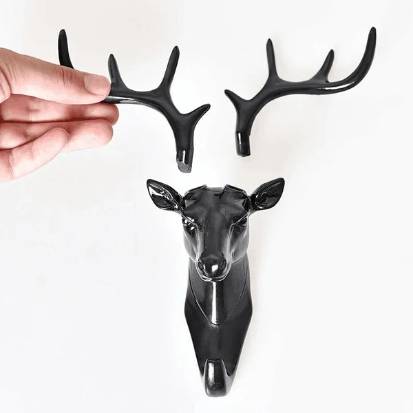 A black vintage deer head wall hook for accessories is shown being held by a hand.
