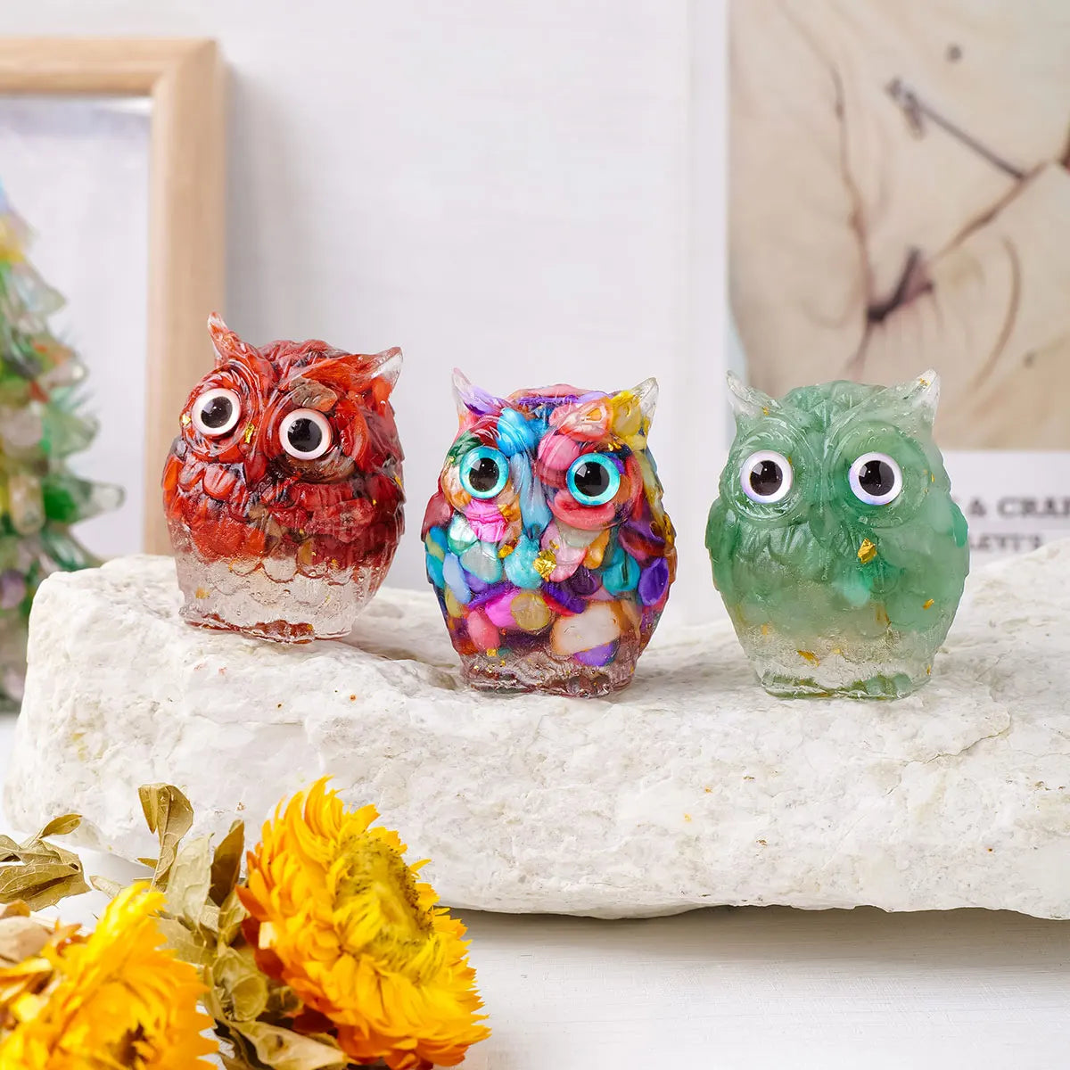 Tres ornamentos de búho hechos de piedra cristalina triturada y colorida goteando sobre una roca blanca.