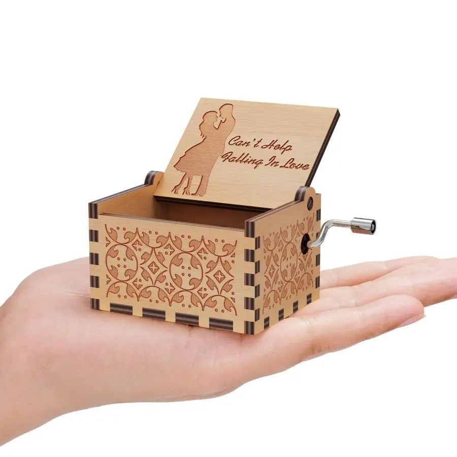 A wooden music box with an engraved silhouette of a couple inside, held in a hand.