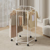 A white rotating hexagon clothes rack with wooden hangers displaying various garments in a bright indoor setting.