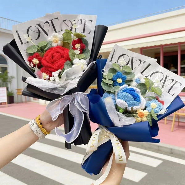 A hand holds a bouquet of artificial roses with green and red flowers wrapped in white paper and blue fabric.