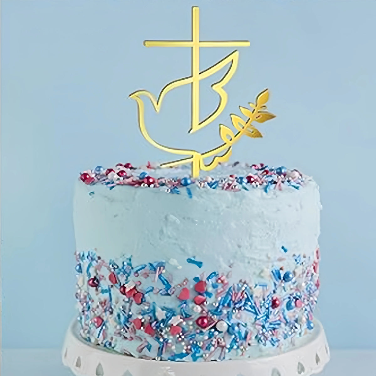 A light blue frosted cake decorated with colorful sprinkles and a gold acrylic cross topper.
