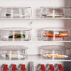 A display of clear microwave splatter guards with heat-resistant handles, holding various food items on a white shelf.
