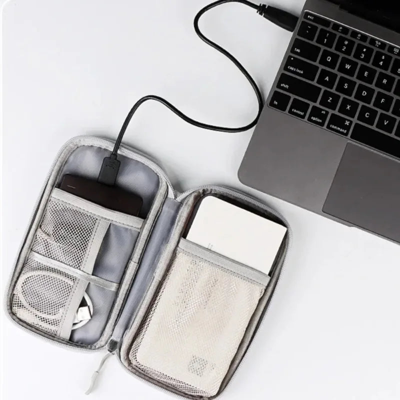 A gray multi-purpose travel electronics organizer bag is open, showing compartments for a pen and a white card next to a lapt