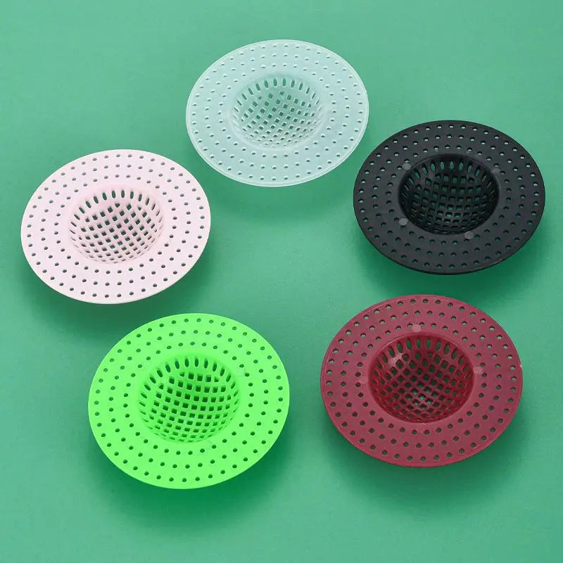 Five colored kitchen sink drain strainers or hair catchers arranged on a green surface.