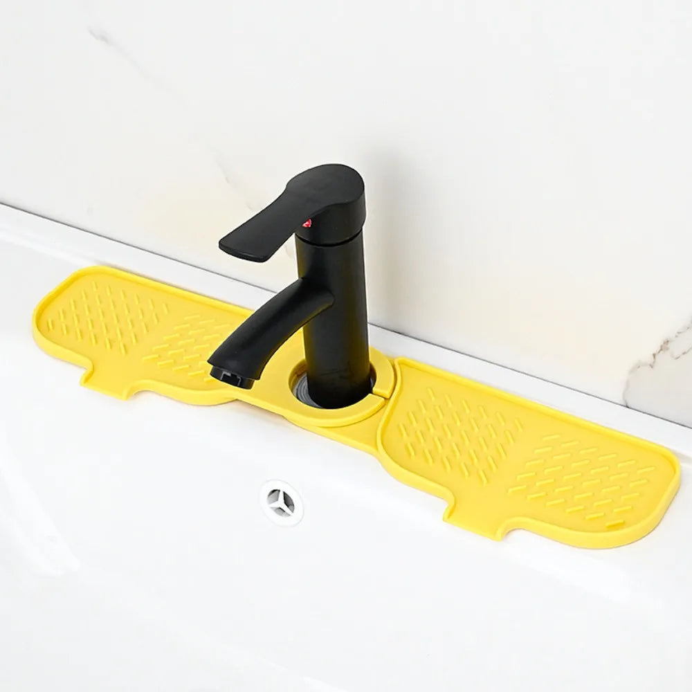 A black flexible silicone sink splash guard drip catcher mat with a handle is placed on a white kitchen sink.