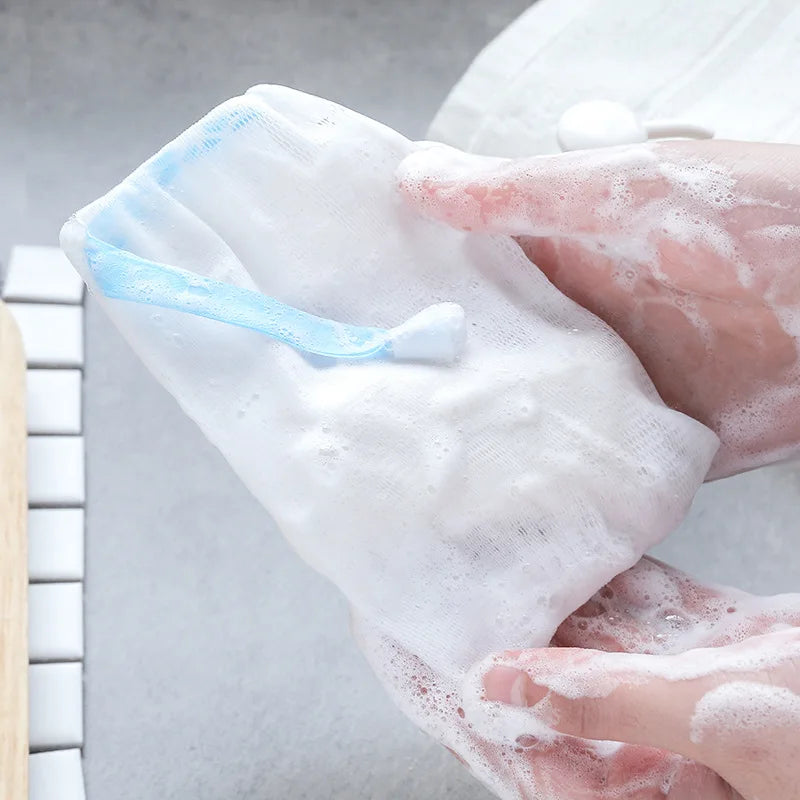 Hands are squeezing a white mesh soap pouch with a blue applicator for gentle exfoliation.