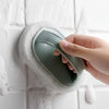 A hand is holding a green magic sponge scrubber with an ergonomic handle against a white tiled surface.
