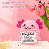 A pink handmade crochet axolotl figurine with pink frills sits on a white surface.