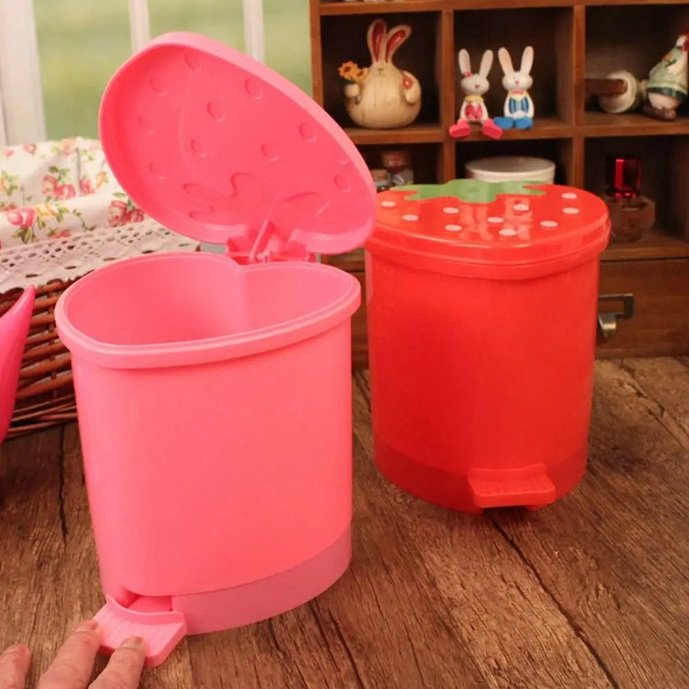 Pinker wiederverwendbarer Erdbeer-Dekor-Mülleimer neben einem roten auf Holzoberfläche.