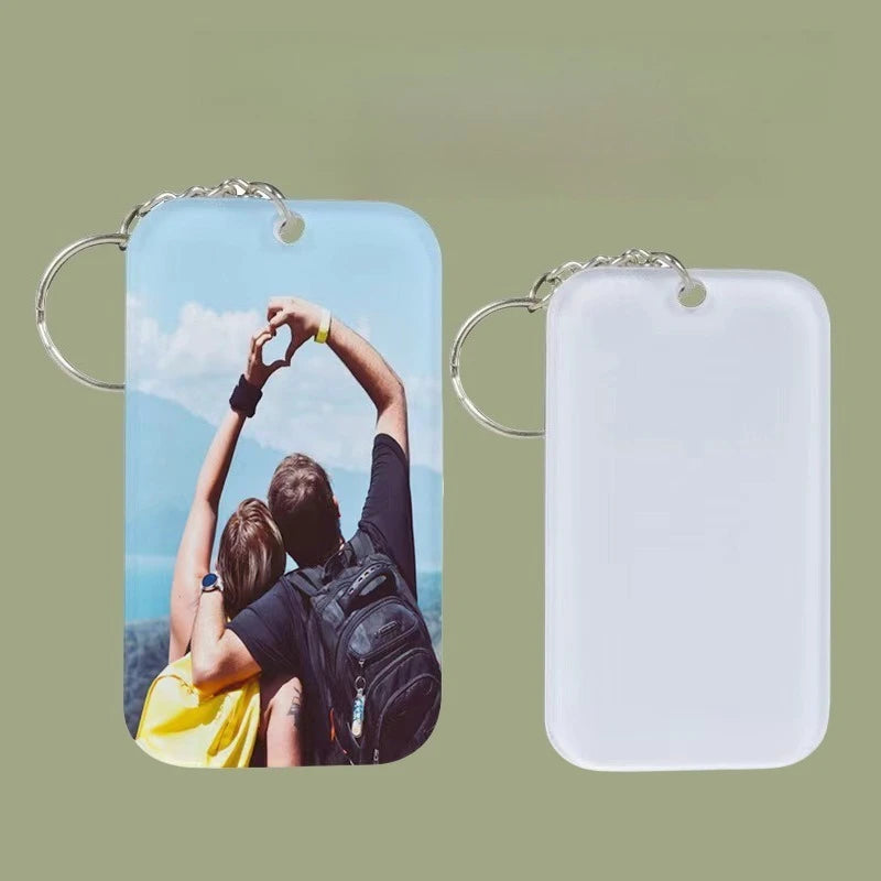 A clear acrylic keychain featuring a photo of a person raising their hands in a heart shape against a blue sky.