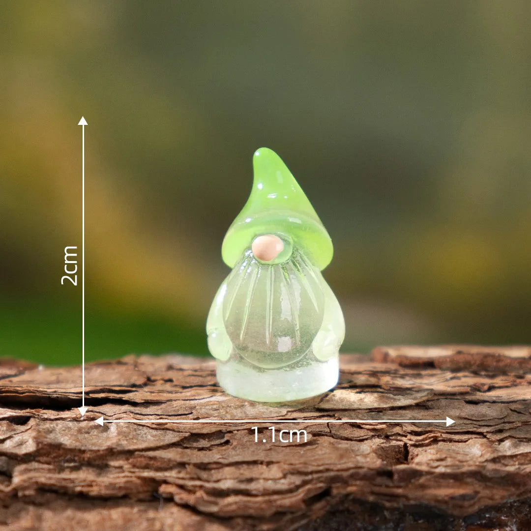 A small, translucent green resin fairy gnome with a pointed hat and a pink nose sits on a piece of wood.
