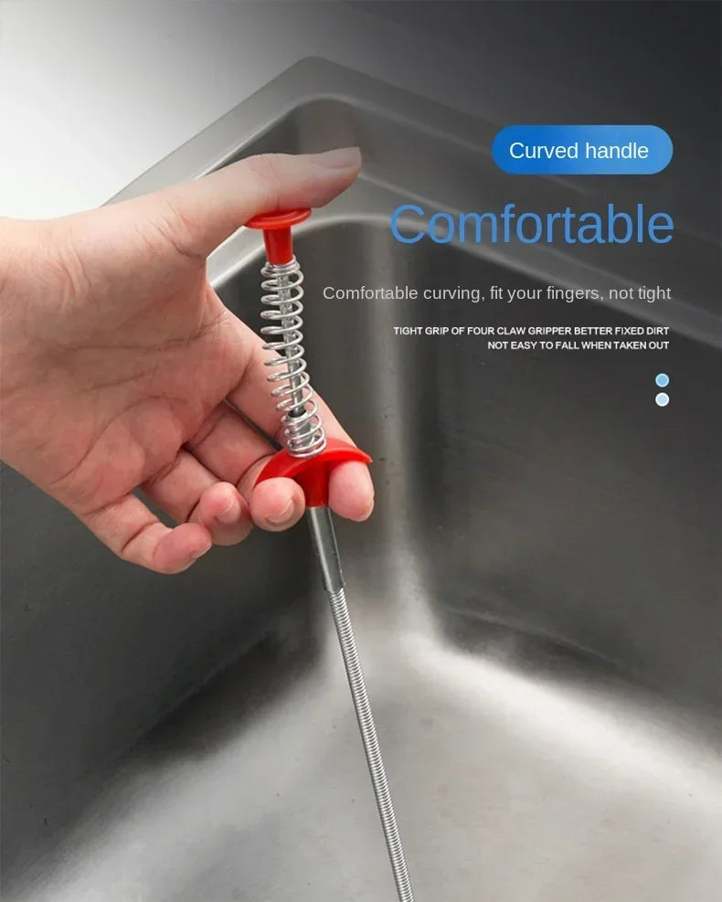A hand is gripping a red, coiled sink and drain unclogging tool with a curved handle inside a metal kitchen sink.