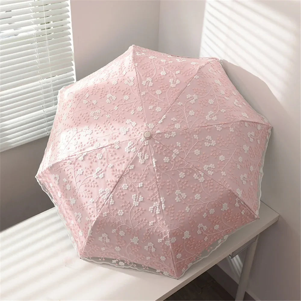 A pink full-automatic embroidered sun umbrella resting on a white surface next to a window.