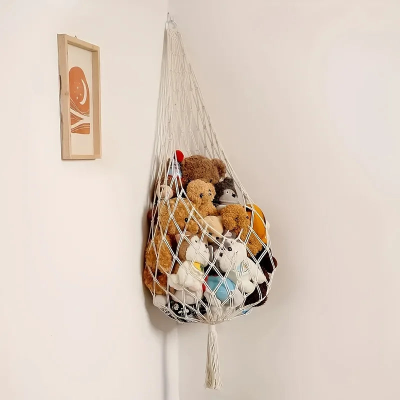 A macrame stuffed animal storage hammock hanging on a white wall, filled with various soft toys.