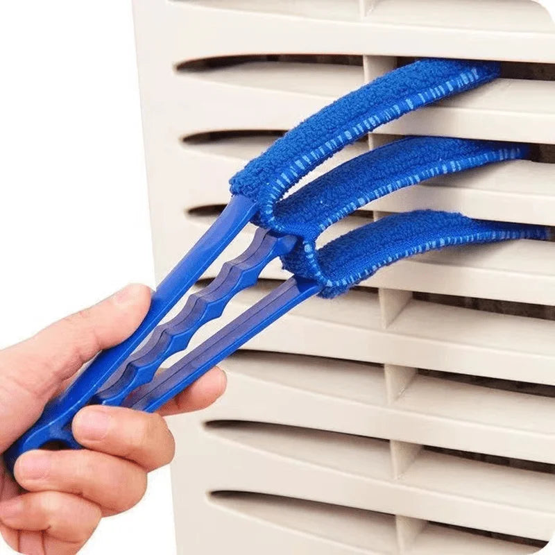 A hand holds a blue reusable household cleaning brush with flexible bristles against a white plastic grate.