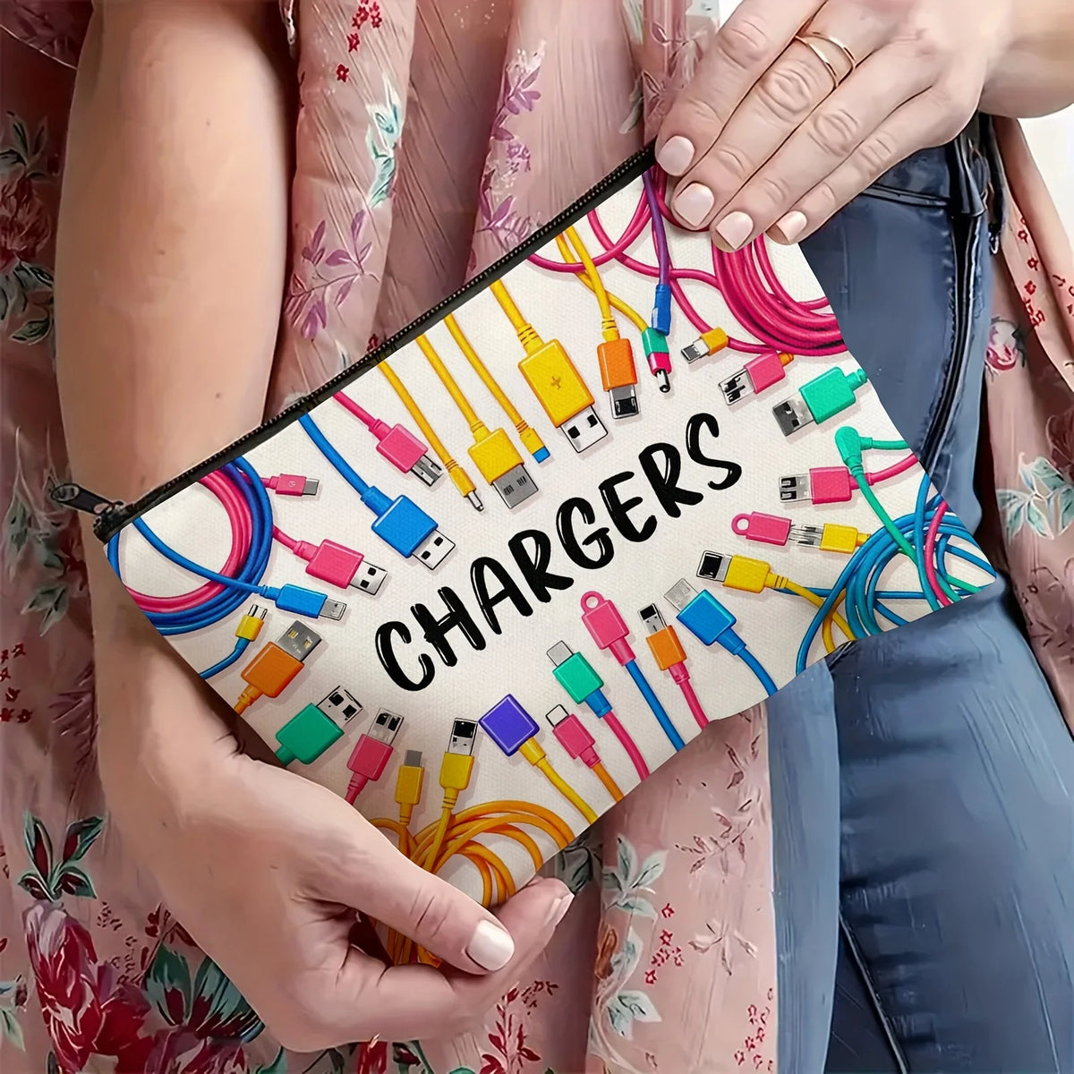 A beige pouch filled with various charging cables and adapters is held by a person wearing a pink floral garment.