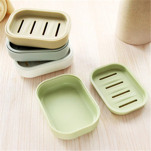 A set of light green and beige compact travel soap cases stacked and displayed on a wooden surface.