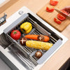 Extendable stainless steel sink drain basket holding various fruits and vegetables like tomatoes, peppers, carrots, and corn